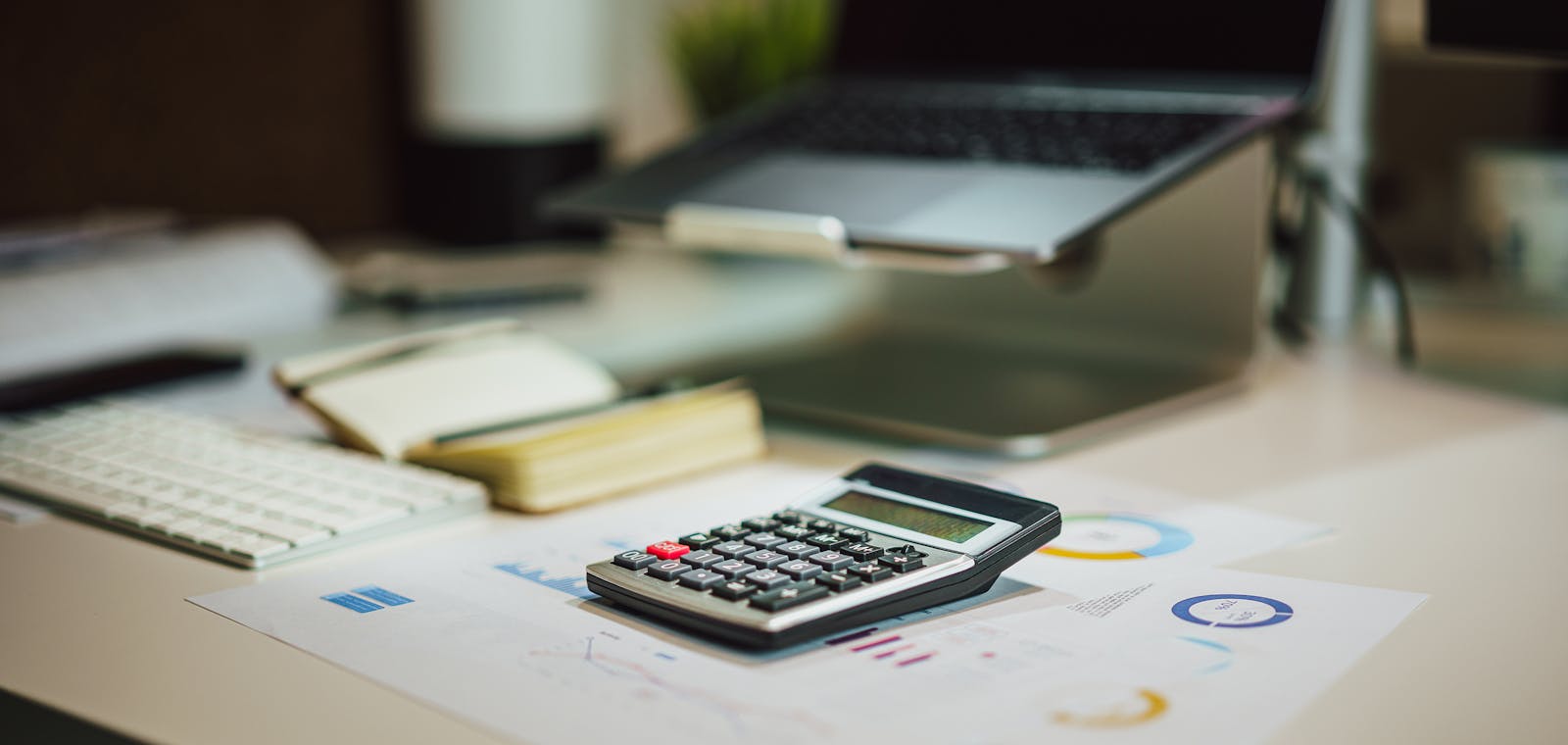 Clean bookkeeping workspace with calculator, reports, laptop, and notebook